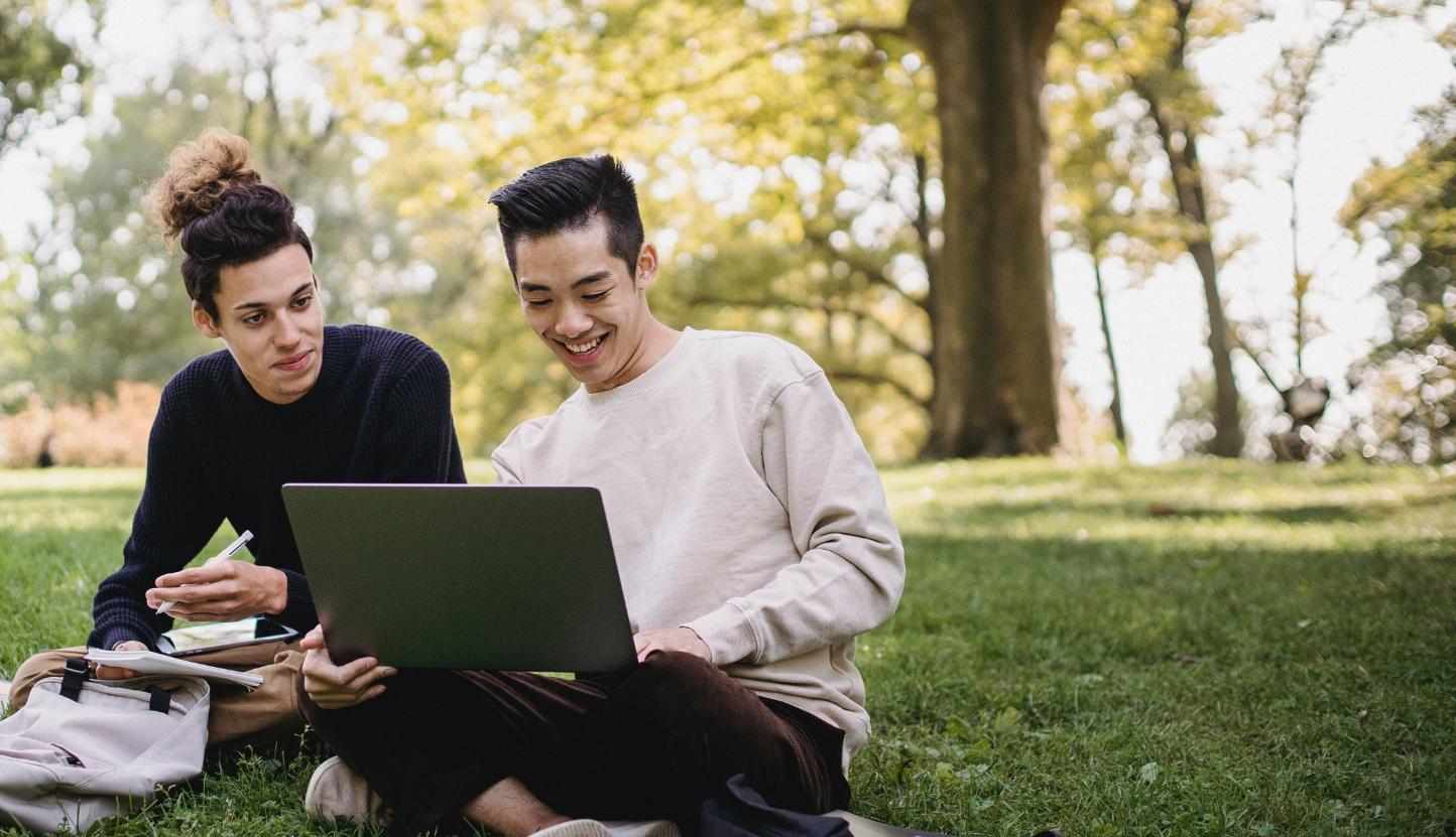 十大网络娱乐平台注册学生看着笔记本电脑，在草坪上聊天.